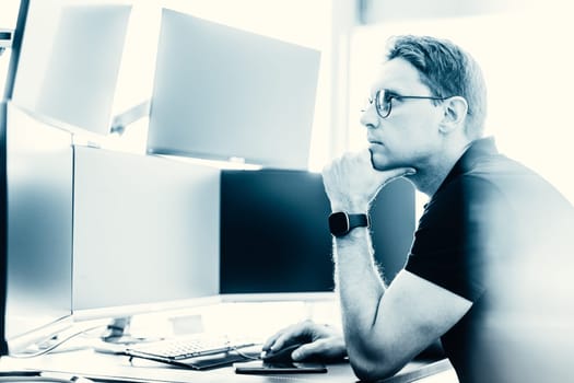 Male stock broker trading online watching charts and data analyses on multiple computer screens.