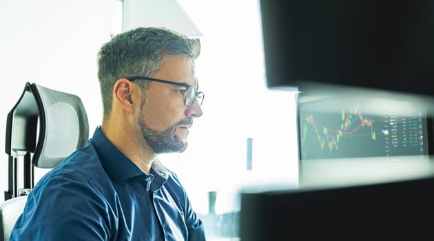 Male stock broker trading online watching charts and data analyses on multiple computer screens.