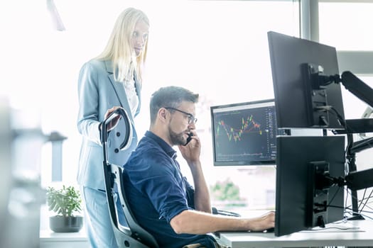 Stock broker business team trading online watching charts and data analyses on multiple computer screens in modern corporate work station office