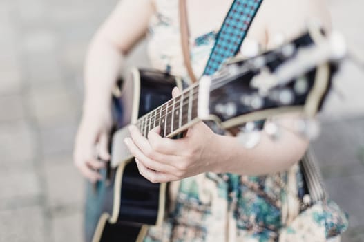 Female street musician playing guitar on sidewalk.