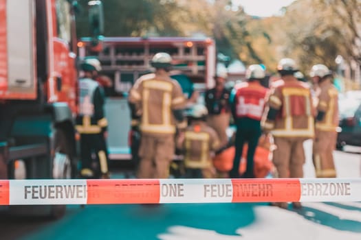 Team of blured firefighters by firetruck on protected accident site. Focus on red and white security band.