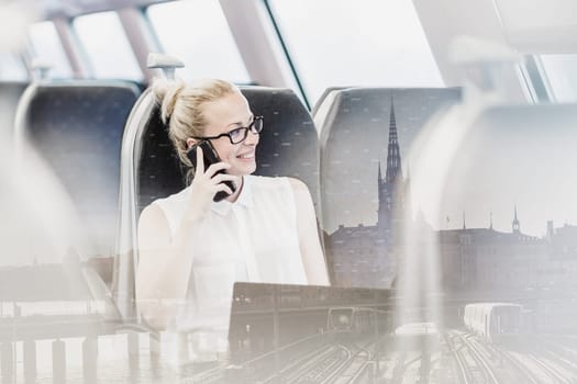Businesswoman talking on cellphone and working on laptop while traveling by train. Business travel concept.