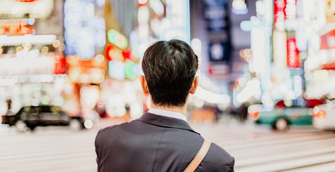 Solitary japanese corporative businessman in suit, after work, waiting on crossroad in Kabukicho, entertainment and red-light district in Shinjuku, Tokyo, Japan.