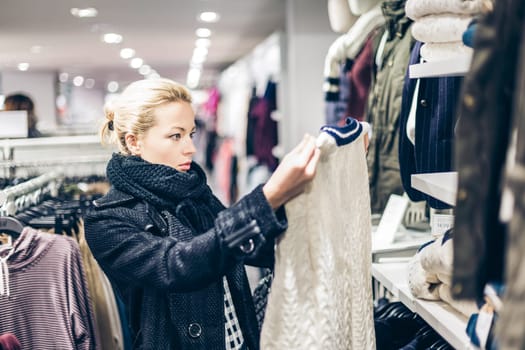 Woman shopping clothes. Shopper looking at clothing indoors in store. Beautiful blonde caucasian female model.