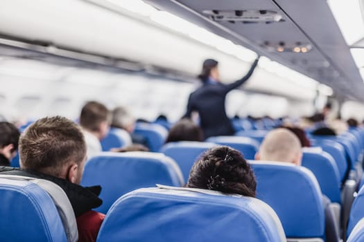 Interior of airplane with passengers on seats and stewardess walking the aisle.