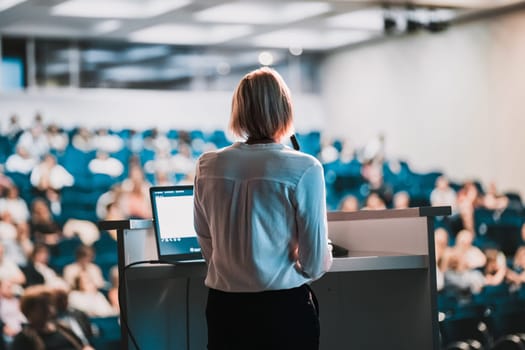 Female speaker giving a talk on corporate business conference. Unrecognizable people in audience at conference hall. Business and Entrepreneurship event