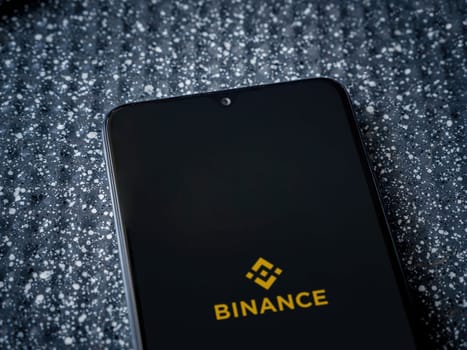 Lod, Israel - July 16,2023: Binance app launch screen on smartphone on metallic background. Close up top view flat lay.