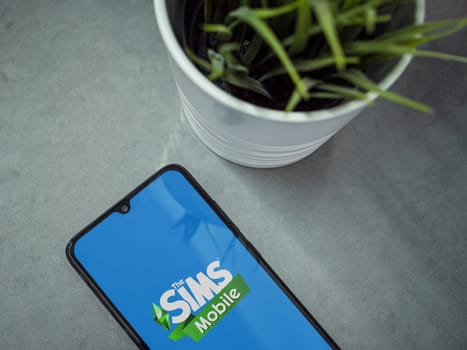 Lod, Israel - July 16,2023: Modern workspace with smartphone with The Sims Mobile app launch screen on marble background. Close up top view flat lay.