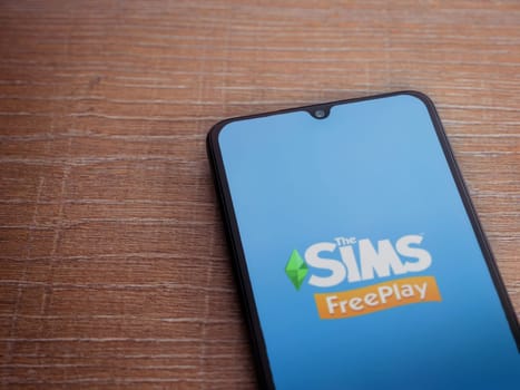 Lod, Israel - July 16,2023: The Sims FreePlay app launch screen on smartphone on wooden background. Top view flat lay with copy space.