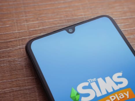Lod, Israel - July 16,2023: The Sims FreePlay app launch screen on smartphone on wooden background. Top view flat lay with copy space.