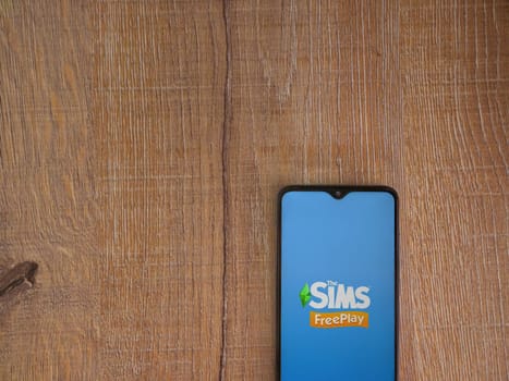 Lod, Israel - July 16,2023: The Sims FreePlay app launch screen on smartphone on wooden background. Top view flat lay with copy space.