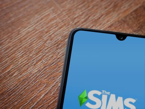Lod, Israel - July 16,2023: The Sims FreePlay app launch screen on smartphone on wooden background. Top view flat lay with copy space.