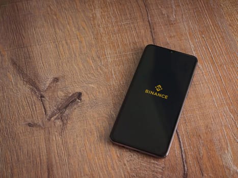 Lod, Israel - July 16,2023: Binance app launch screen on smartphone on wooden background. Top view flat lay with copy space.