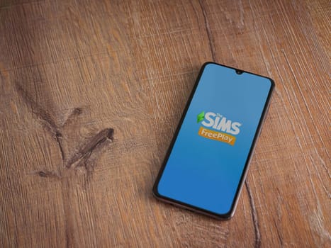 Lod, Israel - July 16,2023: The Sims FreePlay app launch screen on smartphone on wooden background. Top view flat lay with copy space.