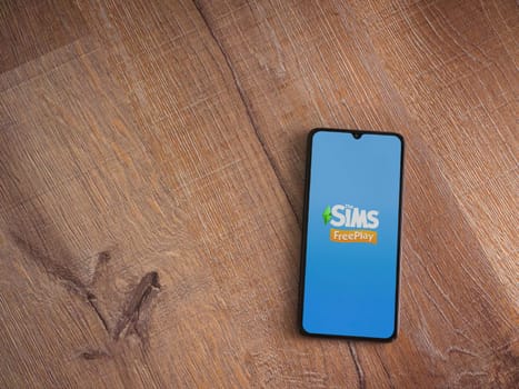 Lod, Israel - July 16,2023: The Sims FreePlay app launch screen on smartphone on wooden background. Top view flat lay with copy space.