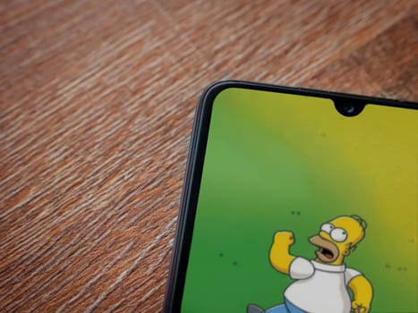 Lod, Israel - July 16,2023: The Simpsons Tapped Out app launch screen on smartphone on wooden background. Top view flat lay with copy space.