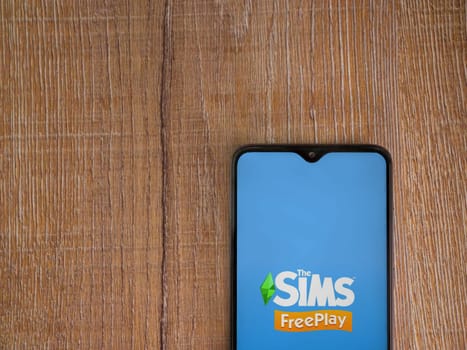 Lod, Israel - July 16,2023: The Sims FreePlay app launch screen on smartphone on wooden background. Top view flat lay with copy space.