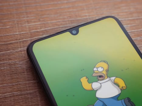 Lod, Israel - July 16,2023: The Simpsons Tapped Out app launch screen on smartphone on wooden background. Top view flat lay with copy space.