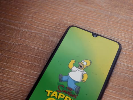 Lod, Israel - July 16,2023: The Simpsons Tapped Out app launch screen on smartphone on wooden background. Top view flat lay with copy space.