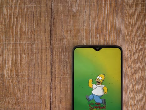 Lod, Israel - July 16,2023: The Simpsons Tapped Out app launch screen on smartphone on wooden background. Top view flat lay with copy space.