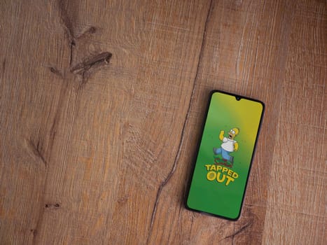 Lod, Israel - July 16,2023: The Simpsons Tapped Out app launch screen on smartphone on wooden background. Top view flat lay with copy space.