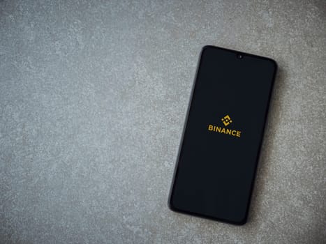 Lod, Israel - July 16,2023: Binance app launch screen on smartphone on ceramic stone background. Top view flat lay with copy space.