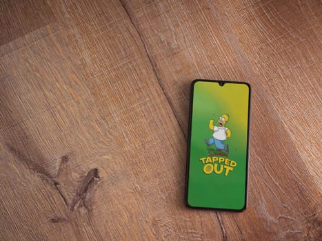 Lod, Israel - July 16,2023: The Simpsons Tapped Out app launch screen on smartphone on wooden background. Top view flat lay with copy space.