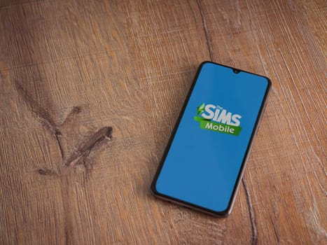 Lod, Israel - July 16,2023: The Sims Mobile app launch screen on smartphone on wooden background. Top view flat lay with copy space.