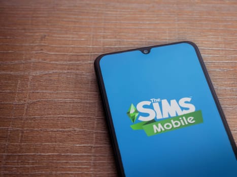Lod, Israel - July 16,2023: The Sims Mobile app launch screen on smartphone on wooden background. Top view flat lay with copy space.