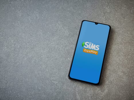 Lod, Israel - July 16,2023: The Sims FreePlay app launch screen on smartphone on ceramic stone background. Top view flat lay with copy space.