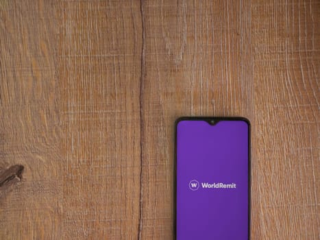 Lod, Israel - July 16,2023: WorldRemit app launch screen on smartphone on wooden background. Top view flat lay with copy space.