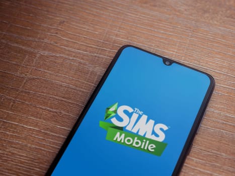 Lod, Israel - July 16,2023: The Sims Mobile app launch screen on smartphone on wooden background. Top view flat lay with copy space.