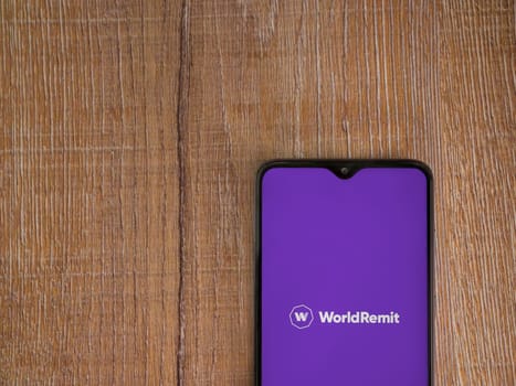 Lod, Israel - July 16,2023: WorldRemit app launch screen on smartphone on wooden background. Top view flat lay with copy space.