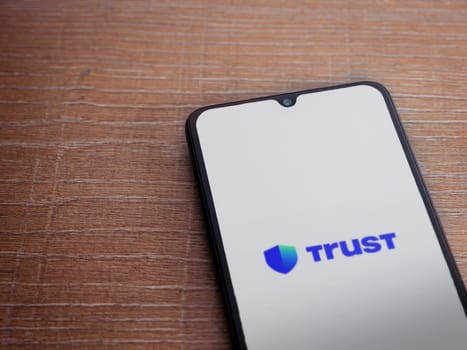 Lod, Israel - July 16,2023: Trust Wallet app launch screen on smartphone on wooden background. Top view flat lay with copy space.