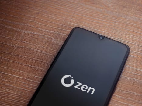 Lod, Israel - July 16,2023: ZEN.COM app launch screen on smartphone on wooden background. Top view flat lay with copy space.