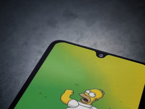 Lod, Israel - July 16,2023: The Simpsons Tapped Out app launch screen on smartphone on dark marble stone background. Top view flat lay with copy space.
