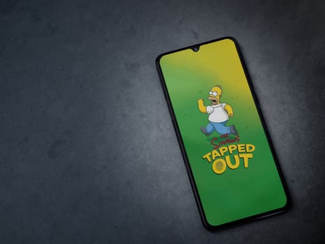 Lod, Israel - July 16,2023: The Simpsons Tapped Out app launch screen on smartphone on dark marble stone background. Top view flat lay with copy space.