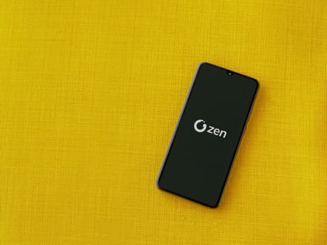 Lod, Israel - July 16,2023: ZEN.COM app launch screen on smartphone on yellow fabric background. Top view flat lay with copy space.