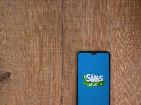 Lod, Israel - July 16,2023: The Sims Mobile app launch screen on smartphone on wooden background. Top view flat lay with copy space.