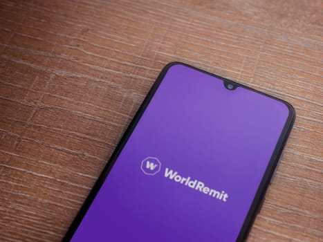 Lod, Israel - July 16,2023: WorldRemit app launch screen on smartphone on wooden background. Top view flat lay with copy space.