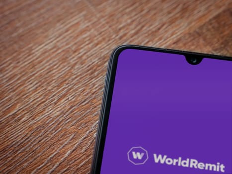Lod, Israel - July 16,2023: WorldRemit app launch screen on smartphone on wooden background. Top view flat lay with copy space.