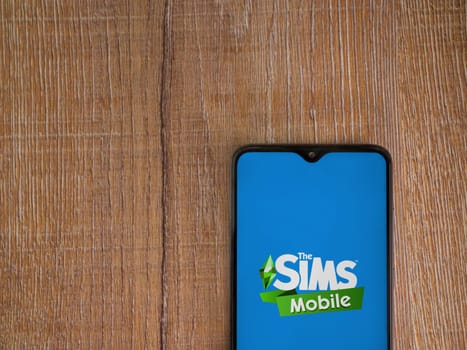 Lod, Israel - July 16,2023: The Sims Mobile app launch screen on smartphone on wooden background. Top view flat lay with copy space.
