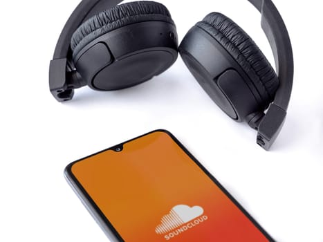 Lod, Israel - July 16,2023: Smartphone with SoundCloud app launch screen and wireless headphones on white background. Top view flat lay with copy space.