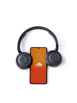 Lod, Israel - July 16,2023: Smartphone with SoundCloud app launch screen and wireless headphones on white background. Top view flat lay with copy space.