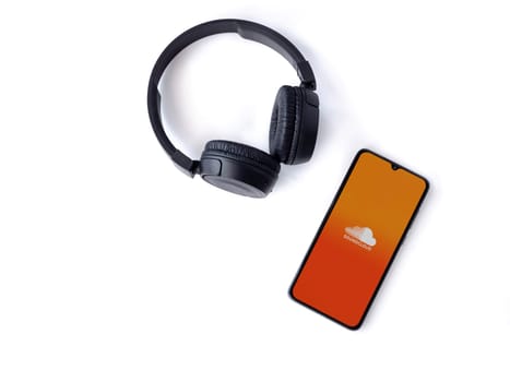 Lod, Israel - July 16,2023: Smartphone with SoundCloud app launch screen and wireless headphones on white background. Top view flat lay with copy space.