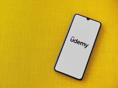 Lod, Israel - July 16,2023: Udemy app launch screen on smartphone on yellow fabric background. Top view flat lay with copy space.