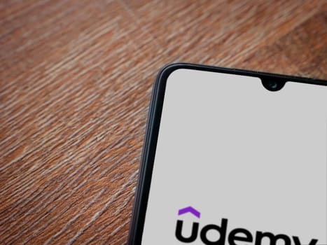 Lod, Israel - July 16,2023: Udemy app launch screen on smartphone on wooden background. Top view flat lay with copy space.