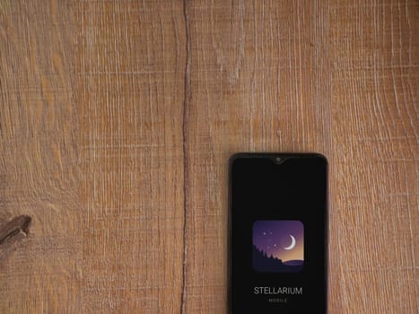 Lod, Israel - July 16,2023: Stellarium - Star Map app launch screen on smartphone on wooden background. Top view flat lay with copy space.