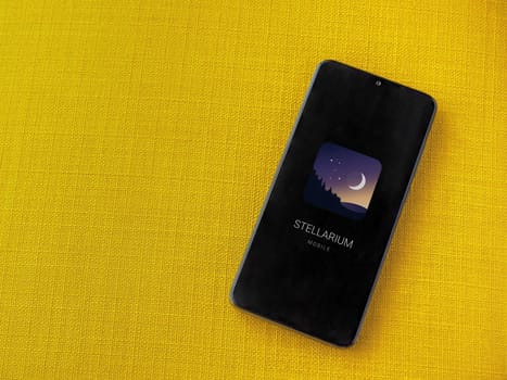 Lod, Israel - July 16,2023: Stellarium - Star Map app launch screen on smartphone on yellow fabric background. Top view flat lay with copy space.