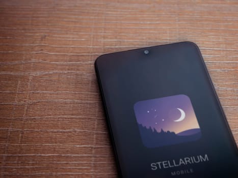 Lod, Israel - July 16,2023: Stellarium - Star Map app launch screen on smartphone on wooden background. Top view flat lay with copy space.